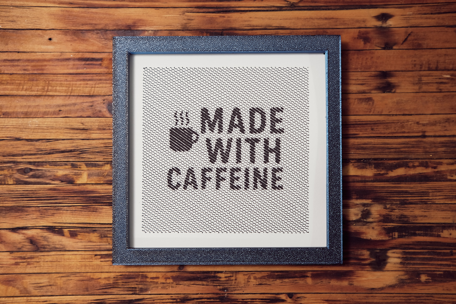 Gerahmtes Plotter-Kunstwerk 'Made with Caffeine' in dunkler Wellentextur, schwarzer Rahmen auf Holz